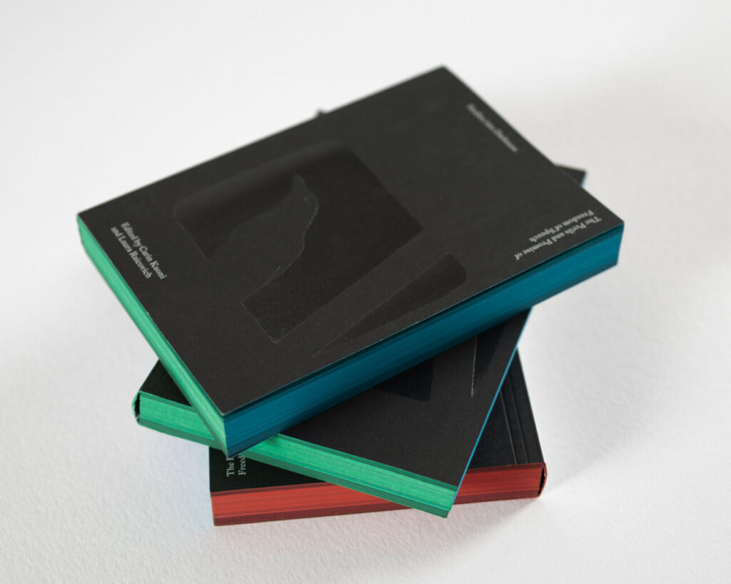 Three identical books with a black cover placed in a stack on a light gray background; white text on the cover reads "Studies into Darkness: The Perils and Promise of Freedom of Speech, edited by Carin Kuoni and Laura Raicovich" in a serif font. Red, blue, and green edge printing.